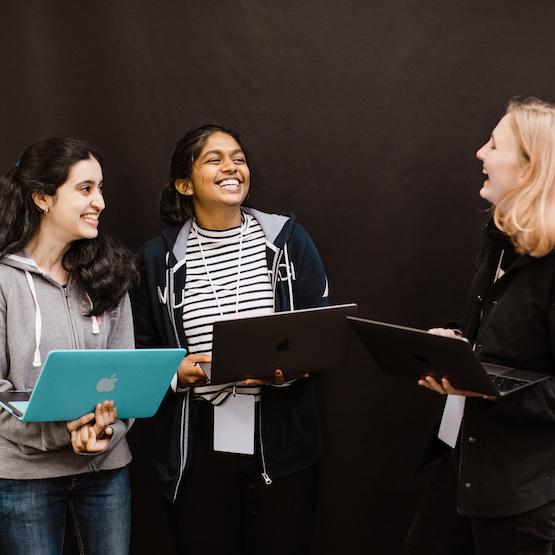 Students laughing with a professor, all holding laptops