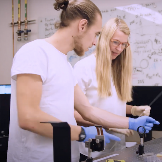 two students in gloves working with electronics in a lab